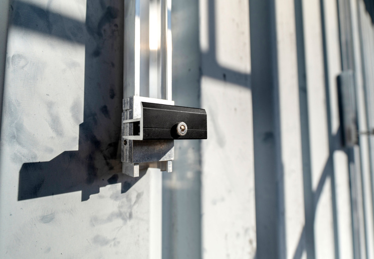 Schwarzes Vorhängeschloss an einer Metall-Servicetür im Sonnenlicht, Symbol für Sicherheit und Zugangskontrolle in der Gebäudetechnik.