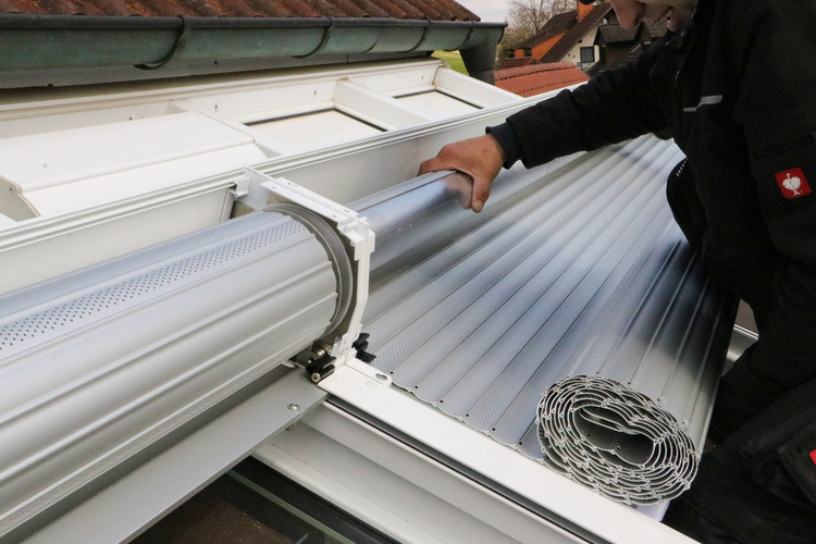 Montage eines Metallrollladens an einem Dachfenster, manuelles Herunterlassen der Lamellen – Einsatz in einer modernen Gebäudehülle.