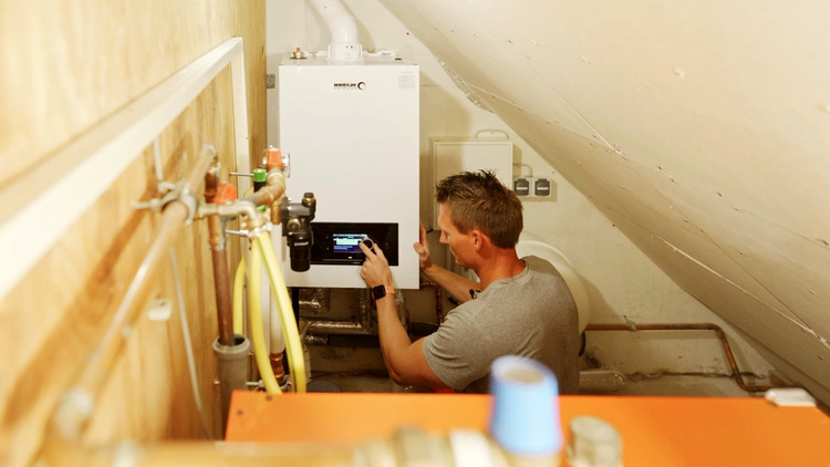 Ein Fachhandwerker installiert einen Heizkessel in einem kompakten, abgeschrägten Technikraum – mit Schwerpunkt auf moderner Gebäudetechnik und Energieeffizienz.