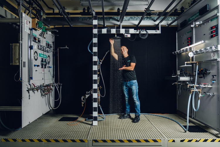 Eine Fachkraft testet in einem Labor eine innovative Sanitärtechnik, indem sie mit einer Säule aus Wassertropfen interagiert; schwarzer Hintergrund.