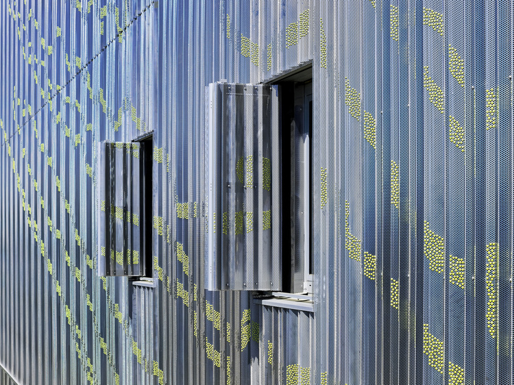 Detailaufnahme einer modernen, perforierten Metallfassade mit zwei offenen rechteckigen Fenstern als Beispiel für eine energieeffiziente Gebäudehülle.
