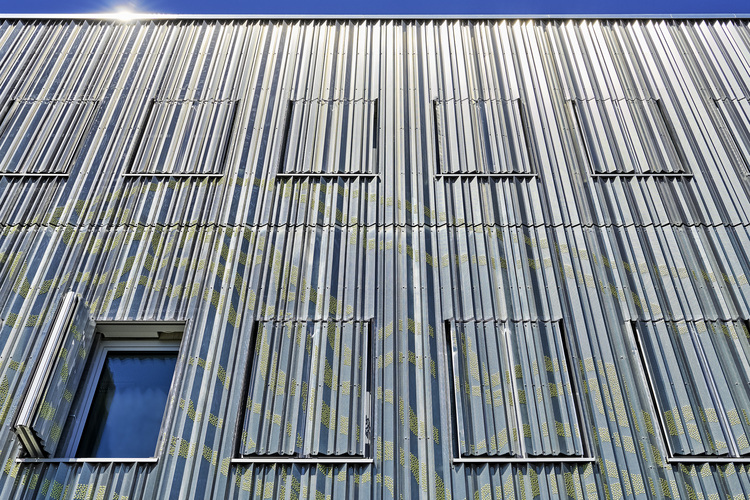 Fassade eines Gebäudes mit Trapezblechprofil, ein geöffnetes Fenster und mehrere geschlossene Fensterläden bei starker Sonneneinstrahlung.