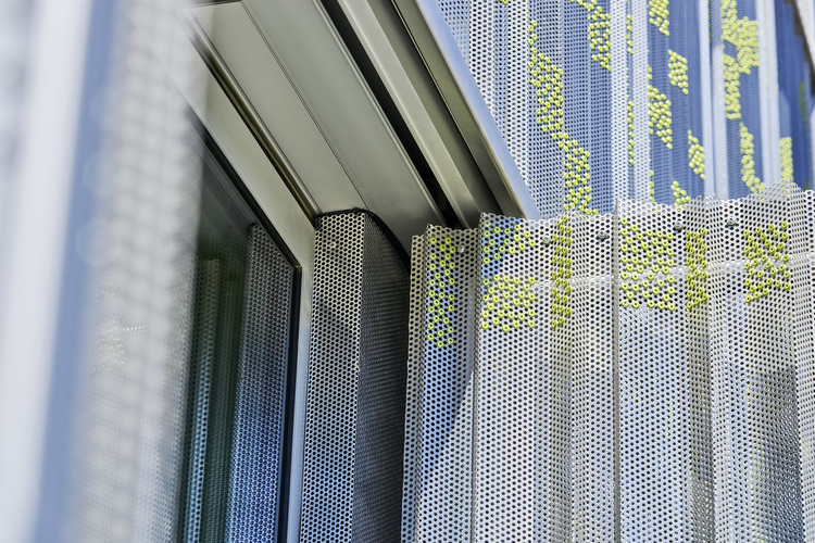 Detailansicht einer modernen Gebäudehülle mit perforierten Metallpaneelen und Glasflächen, die Energieeffizienz und moderne Fassadentechnik veranschaulichen.