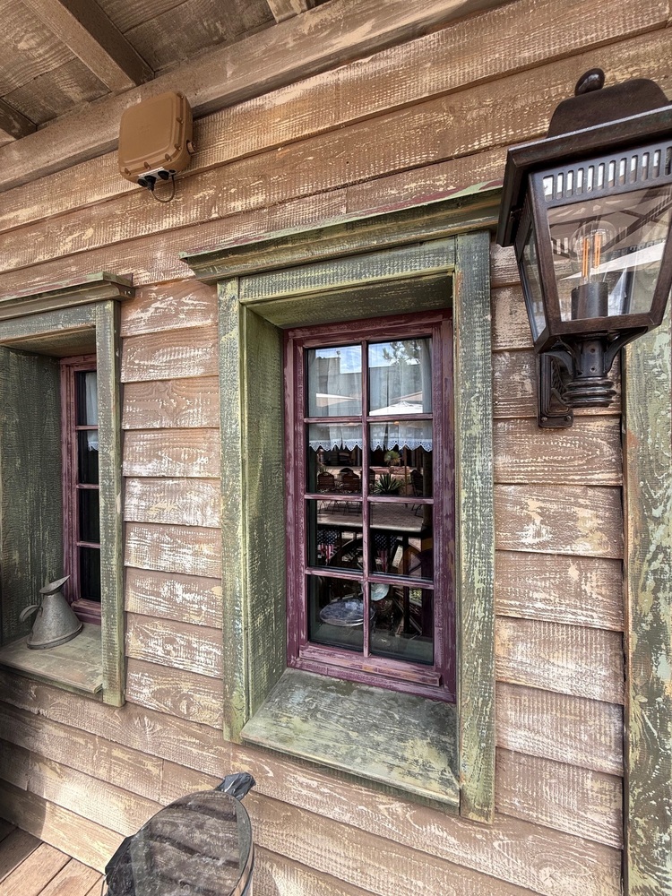 Holzfassade mit zwei Fenstern, einer Laterne und einem Metallkrug – beispielhafte Gebäudehülle für eine energetische Sanierung.
