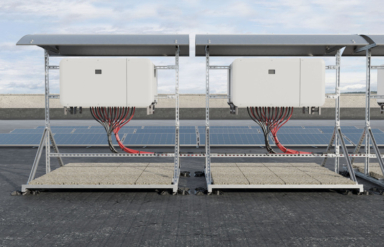 Zwei weiße Wechselrichter mit Kabeln auf Metallgestellen vor Photovoltaikmodulen als Teil einer PV-Anlage zur Energieversorgung im Außenbereich.