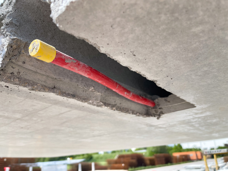 Ein Rohr mit roter Kappe ragt aus einer rechteckigen Öffnung in der Betondecke auf einer Baustelle heraus; Detailansicht der Installation im Bereich der Gebäudetechnik.