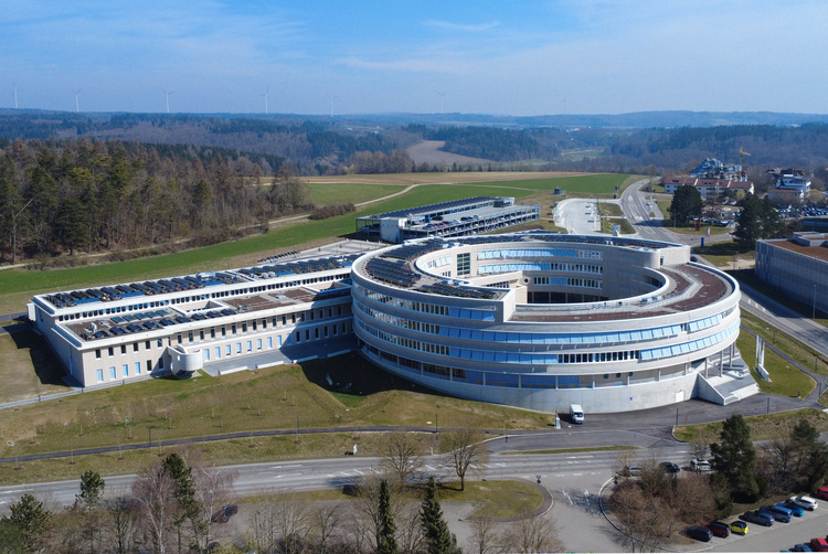 Luftaufnahme eines modernen, runden Gebäudes für Gebäudetechnik, umgeben von Grünflächen und Straßen – geeignet für Fachthemen auf haustec.de.