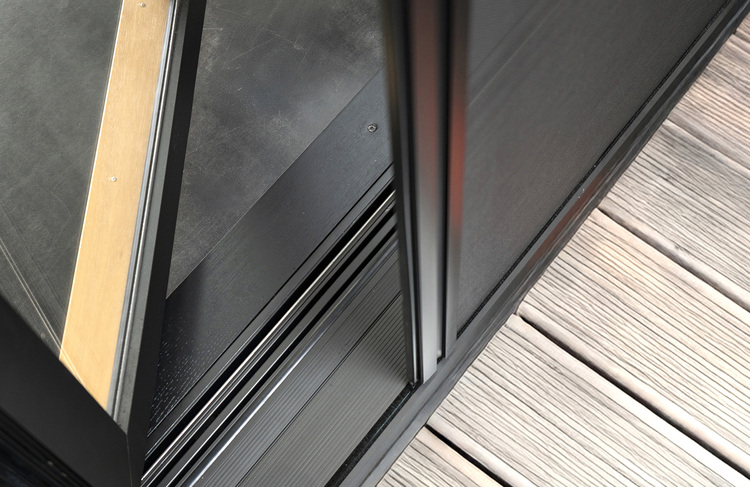 Detailansicht: Teilweise geöffnete Glasschiebetür auf einer Holzterrasse mit Metallschiene, Fokus auf die bodennahen, barrierefreien Türschwelle.