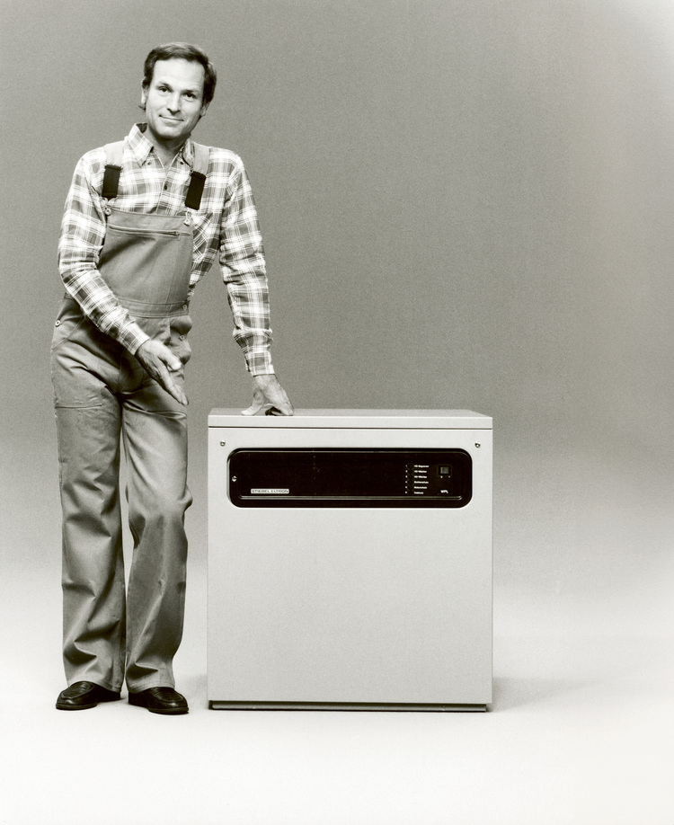 Ein Handwerker in Arbeitskleidung präsentiert einen historischen Computer, ein Symbol für Digitalisierung und Automatisierung in der Gebäudetechnik.