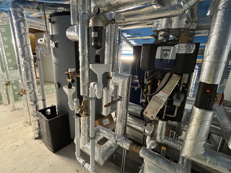 Isolierte Rohrleitungen und zentrale HLK-Komponenten in einem Technikraum mit Betonboden – ein typisches Beispiel für moderne Gebäudetechnik.
