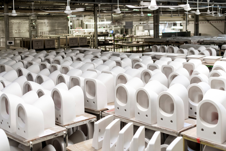 Produktionslinie für Sanitärkeramik: Weiße WC-Spülkästen stehen in Reihen im Fertigungsbereich eines Werks für Gebäudetechnik unter heller Beleuchtung.