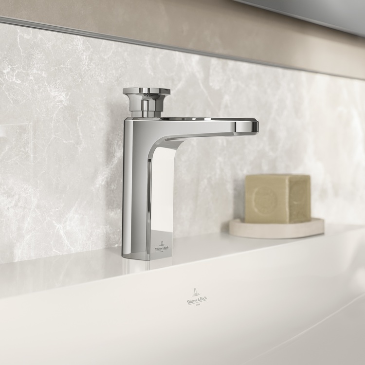 Moderne verchromte Waschtischarmatur an einem weißen Waschbecken, daneben Seife – ein Beispiel für zeitgemäße Sanitärtechnik in einem minimalistischen Badezimmer.