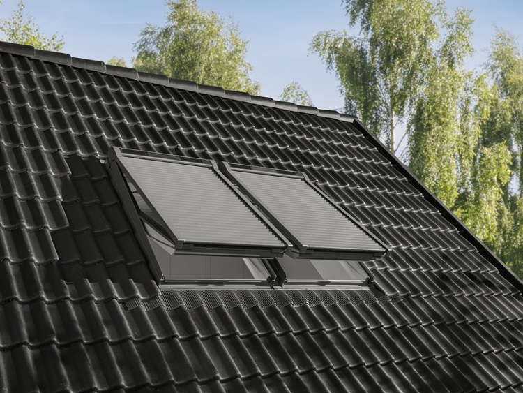 Zwei Dachfenster mit außenliegenden Sonnenschutzvorrichtungen auf schwarzer Dacheindeckung, relevant für energieeffiziente Gebäudehüllen.