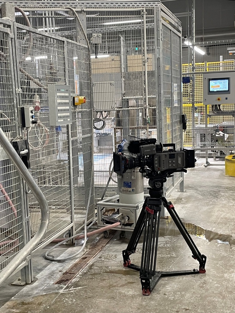 Eine Videokamera auf einem Stativ dokumentiert die Steuerungstechnik und den Aufbau der Anlage in einer modernen Industriehalle für Gebäudetechnik.