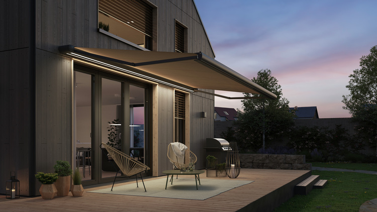 Eine moderne Terrasse in der Abenddämmerung mit zwei Stühlen, einem Outdoor-Teppich, einem Grill und einer großen Markise als Beispiel für eine effiziente Gestaltung des Außenbereichs.