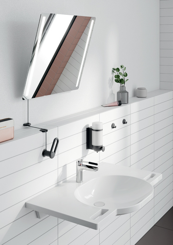 Sanitärraum mit weißem Waschtisch, schrägem Spiegel, Seifenspender und Pflanze vor einer weiß gefliesten Wand – modernes Bad-Design in der Gebäudetechnik.