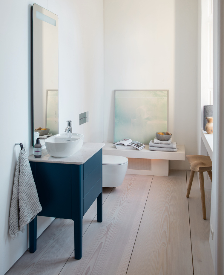 Modernes Badezimmer mit blauer Waschtischanlage, rundem Waschbecken, Wandspiegel und natürlichem Lichteinfall für ein energieeffizientes Design.
