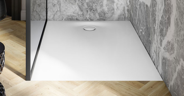 Barrierefreie Dusche mit rutschfester weißer Duschwanne, rundem Abfluss, gläserner Trennwand und fugenarmen Wandpaneelen in Marmoroptik.