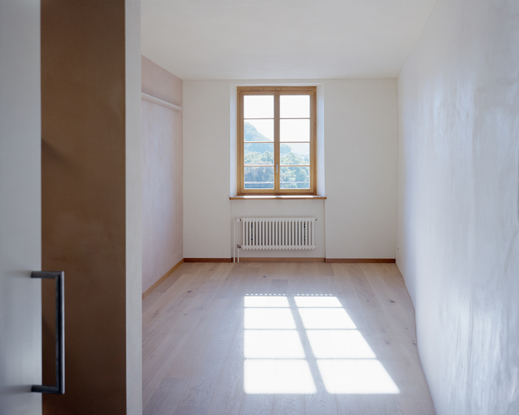 Leerer Raum mit Holzboden, weißen Wänden und Fenstern; das Sonnenlicht verdeutlicht den potenziellen Lichteinfall für eine energieeffiziente Gebäudetechnik.