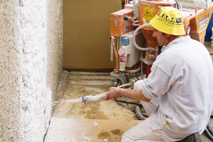 Ein Facharbeiter trägt Spritzputz mit einem Schlauch und einer Putzmaschine auf eine Innenwand auf – moderne Bautechnik für eine effiziente Wandbeschichtung im Hochbau.