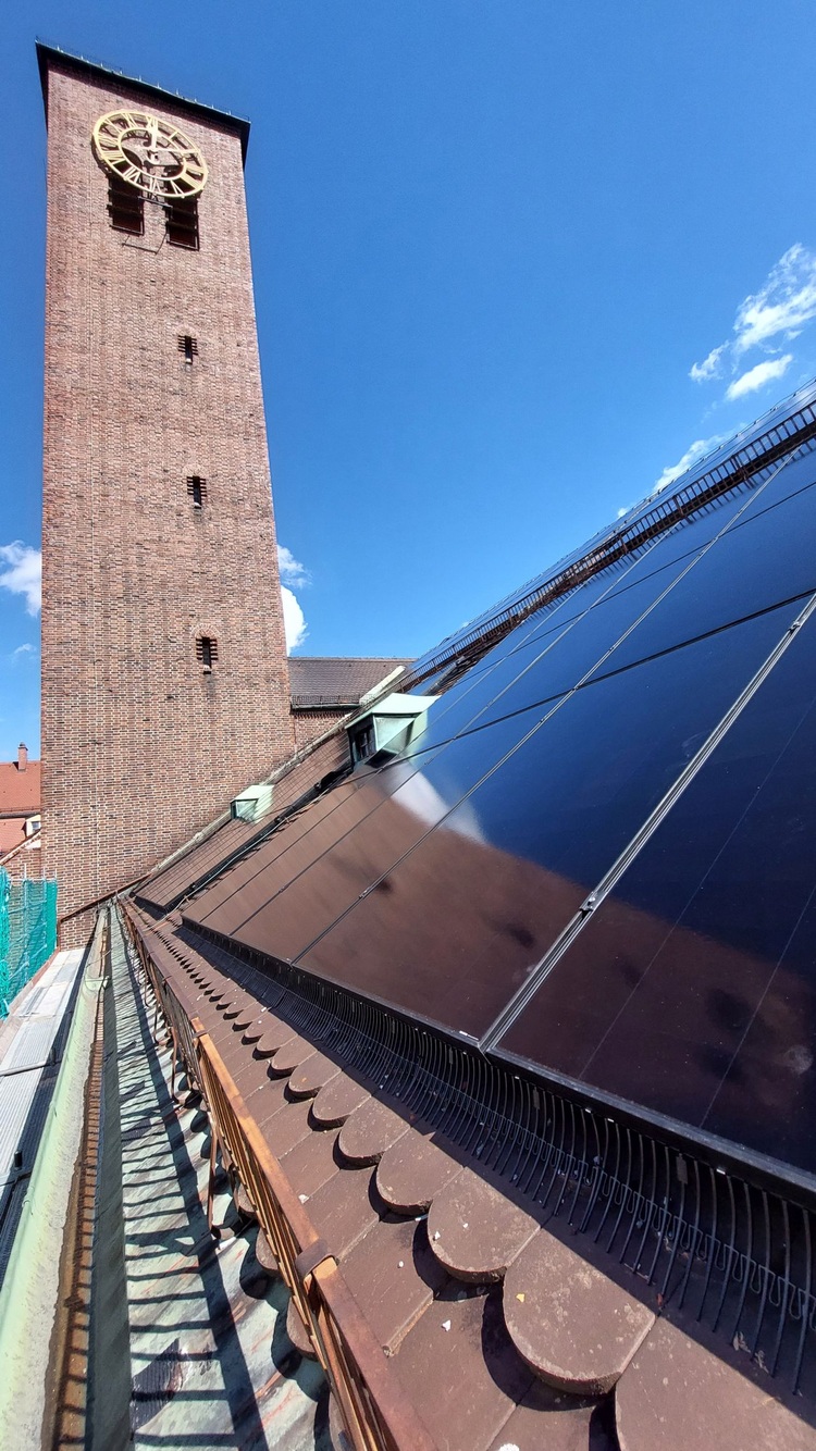 Solarzellen auf einem Gebäudedach neben einem historischen Uhrturm – ein Symbol für die Integration erneuerbarer Energien in die Gebäudetechnik.
