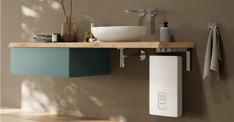 Sanitärinstallation: Modernes Badezimmer mit Aufsatzwaschbecken, Armatur, Handtüchern und Untertischgerät zur Warmwasserbereitung unter der Holzarbeitsplatte.