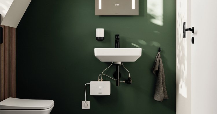 Barrierefreier Sanitärbereich mit kompaktem Waschtisch, sichtbaren Rohrleitungen und einer grünen Akzentwand – moderne Gebäudetechnik.