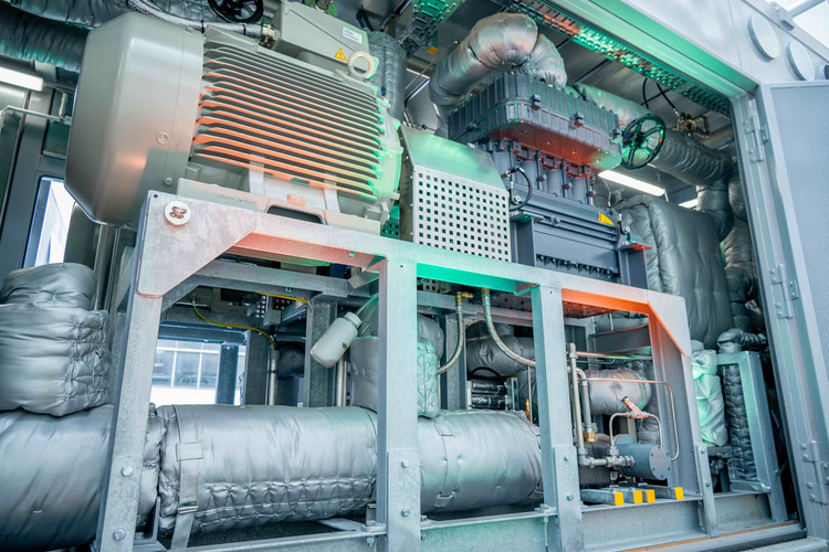 Industriekompressor mit großem Elektromotor und isolierter Verrohrung in einem Metallgehäuse.