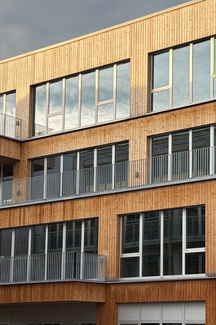 Modernes Holzgebäude mit großen Fenstern und Metallgeländern, ein Beispiel für eine energieeffiziente Gebäudehülle in der Gebäudetechnik.