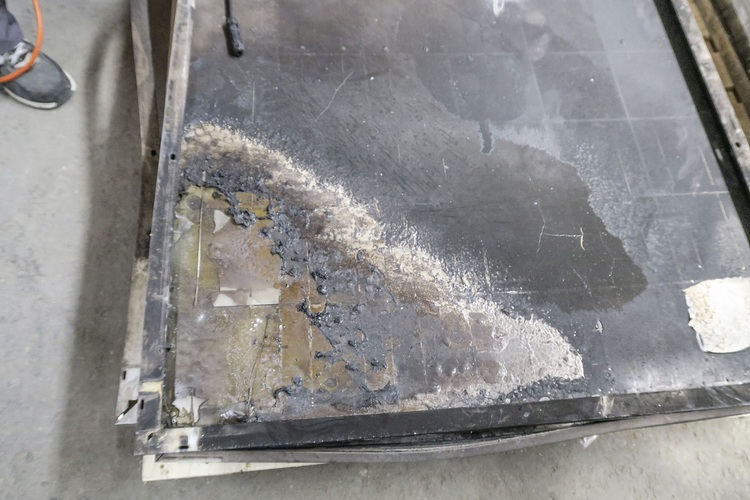 Detailaufnahme eines Flachpaneels mit deutlichen Brand- und Wasserschäden, Verfärbungen und Materialablagerungen, die für die Gebäudetechnik von Bedeutung sind.