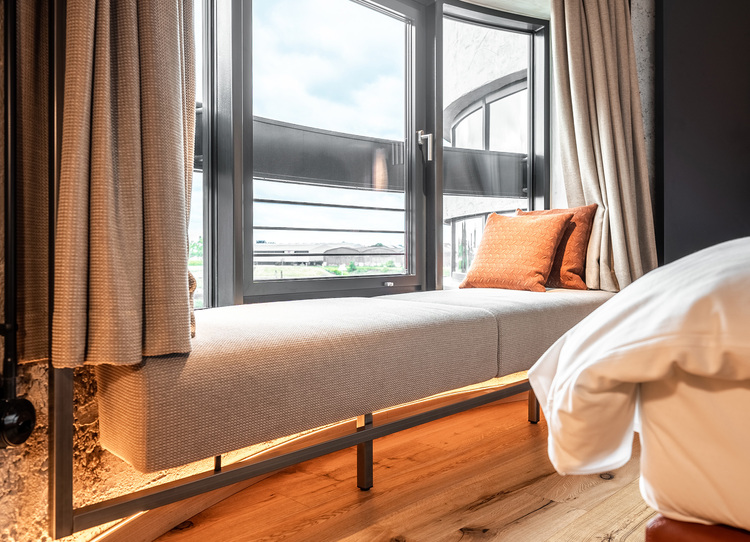 Fensterplatz mit Polstern in einer energieeffizienten Gebäudehülle, der eine fachgerechte Verglasung, Wärmedämmung und moderne Fensterrahmen aufweist.