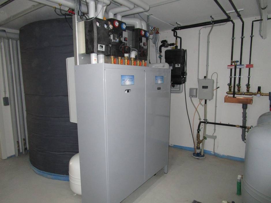 Hier ist im Hintergrund ein 4200-Liter-Pufferspeicher zu sehen. Er ist verbunden mit einer Luftwärmepumpe, die außerhalb des Hauses arbeitet. Der „Wärmemanager“ im Vordergrund sorgt für ein optimiertes Zusammenspiel der Komponenten, welches sich nach dem jeweiligen Angebot an solarer Energie und dem aktuellen Bedarf an Wärme und Haushaltsstrom richtet. Flexible Stromtarife können ebenfalls berücksichtigt werden, sofern sie vom Versorger bereits angeboten werden.