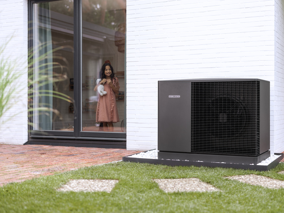 Eine Wärmepumpe steht vor einem Haus in einem Garten.