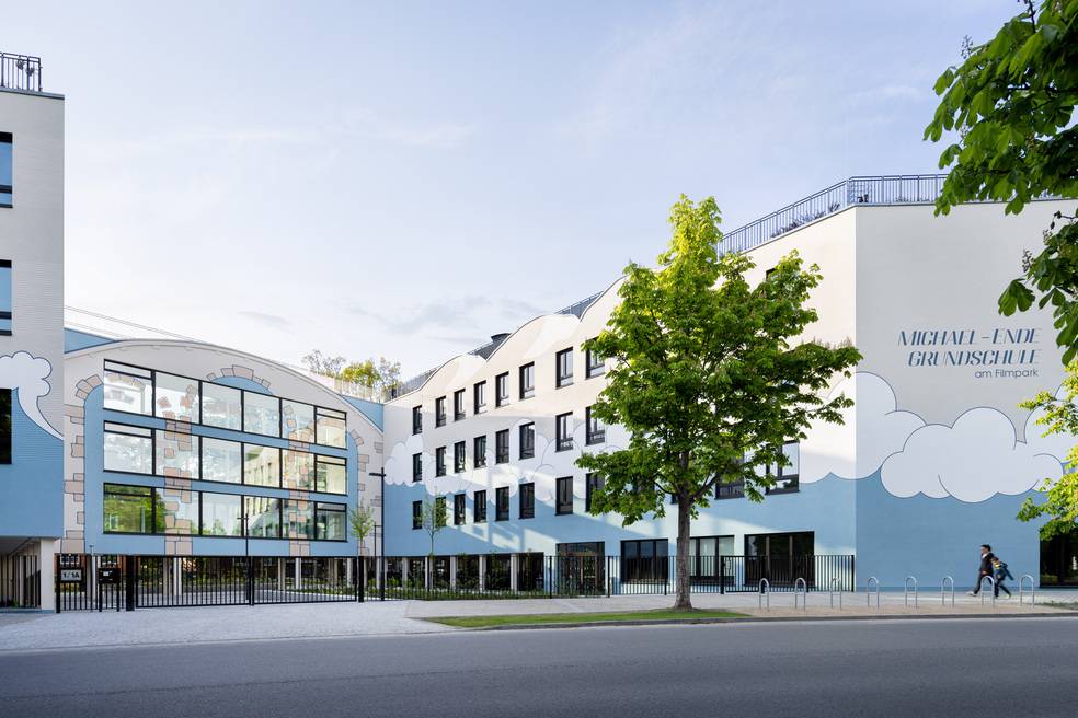 Alt-Text: „Ein modernes Schulgebäude mit energiesparenden großen Fenstern, nachhaltiger Architektur und farbenfrohen Wandpaneelen, umgeben von einer energieeffizienten Landschaftsgestaltung.“.