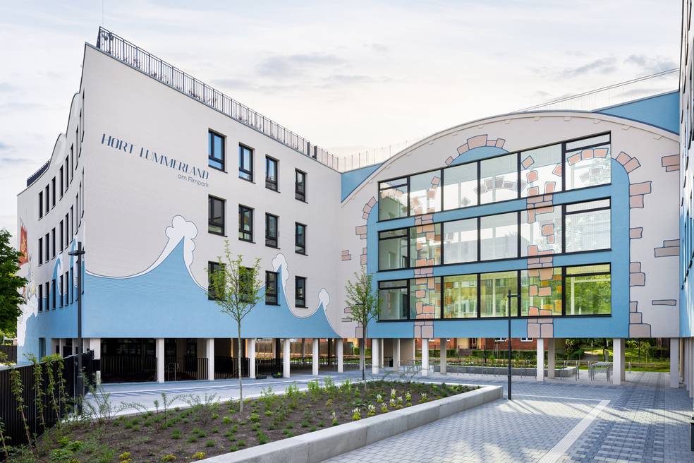 Alt-Text: „Gebäudefassade mit weiß-blauen Paneelen, großen Fenstern und wellenförmigen Designelementen, die Energieeffizienz durch moderne Baumaterialien hervorhebt.“.