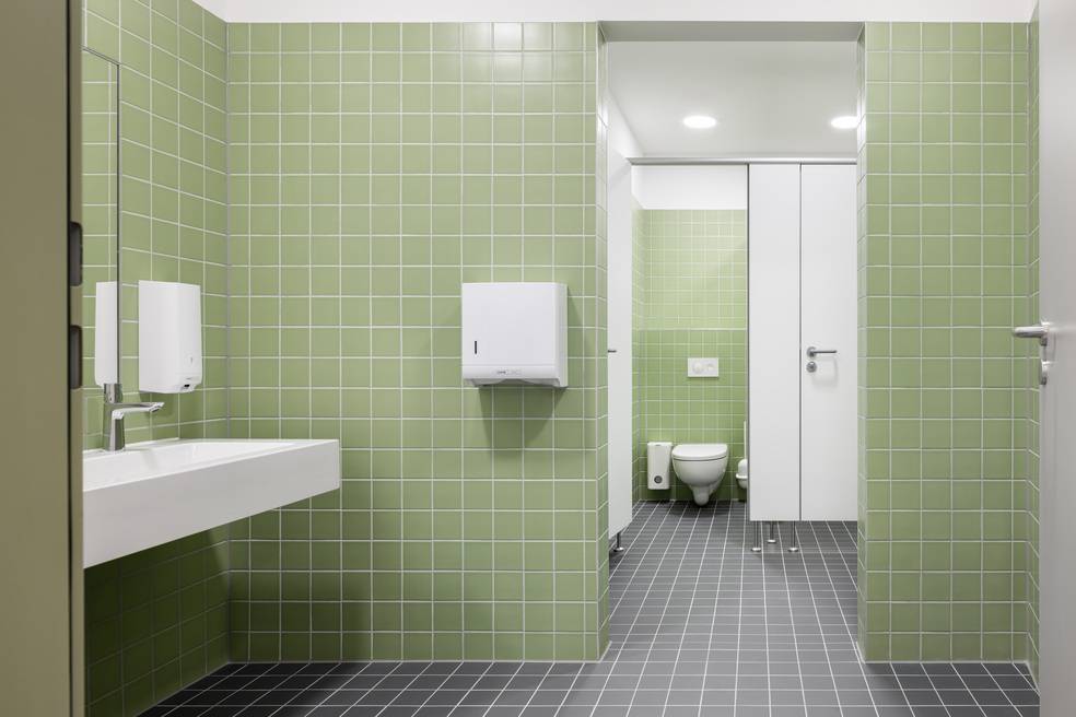 ALT-Text: „Öffentliche Sanitäreinrichtung mit grünen Kachelwänden, einem modernen weißen Waschbecken, einem effizienten Papierhandtuchspender und einer barrierearmen Toilettenkabine.“
Dieser optimierte ALT-Text berücksichtigt die Zielgruppe auf haustec.de und legt den Fokus auf Aspekte wie Modernität und Barrierefreiheit, die für Entscheider in der Gebäudetechnik von Bedeutung sind.