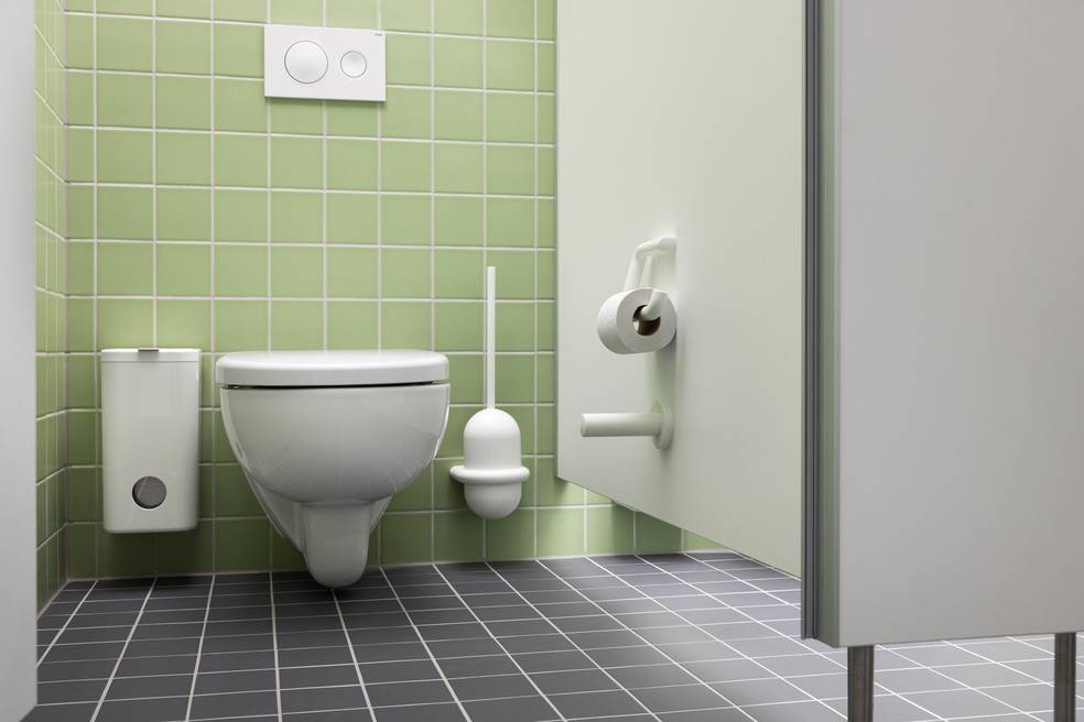 ALT-Text: Modern ausgestattete öffentliche WC-Kabine mit wandmontierter Toilette, innovativer Toilettenbürste und benutzerfreundlichem Toilettenpapierhalter. Die grünen Fliesenwände und der graue Boden betonen die Designästhetik und die einfache Reinigung, ideal für barrierefreie Gebäude in der Sanitärtechnikbranche.