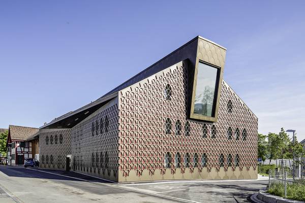 Hinter der filigranen Fassade aus eloxiertem Aluminium zeichnen sich die darunterliegende Fassadenebene und die ovalen Fenster ab. Hinter der filigranen Fassade aus eloxiertem Aluminium zeichnen sich die darunterliegende Fassadenebene und die ovalen Fenster ab.