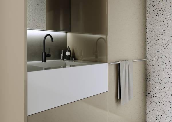 Warme Grau- und Beigetöne kontrastieren dezent mit dem matten Schwarz der Meta Armaturen, hochglänzende Fronten mit der lebendigen, spannungsreichen Textur von Terrazzo. 