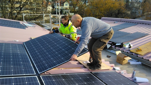 Montageprozess: Installateure verkleben ultraleichte PV-Module auf einem Trapezblechdach.