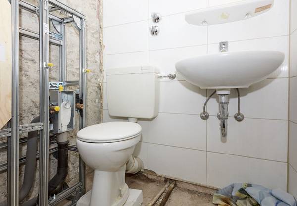 Sanierung im bewohnten Zustand: Während auf der einen Wandseite das Geberit Installationssystem mit Anschlüssen für das neue WC installiert wird, können die Bewohner noch das alte WC und den Waschtisch nutzen.