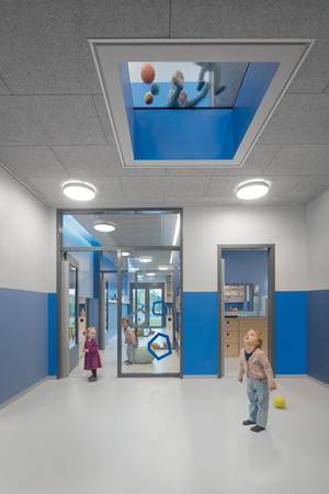 Der Eingangsbereich gibt Orientierung: Von hier aus können die Kinder geradeaus durch die Kita in den Garten und durch das Bodenfenster im Obergeschoss und das in der Verlängerung liegende Dachfenster direkt in den Himmel sehen.