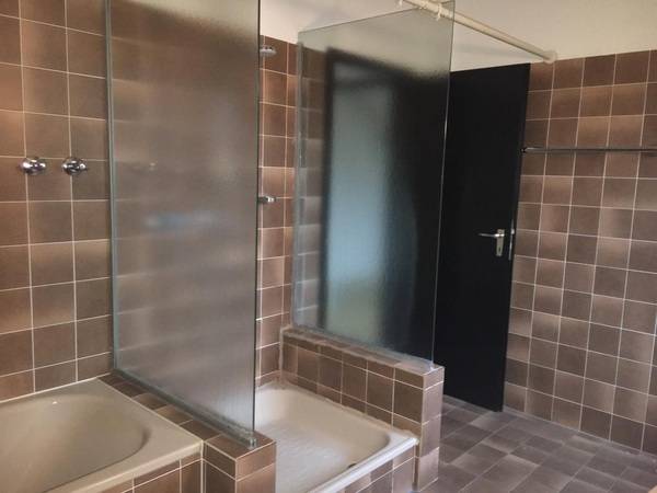 Die Dusche hat einen hohen Sockel, der den Einstieg erschwert. Links und rechts dient eine Abtrennung als Spritzschutz, vorne war ein Duschvorhang befestigt.