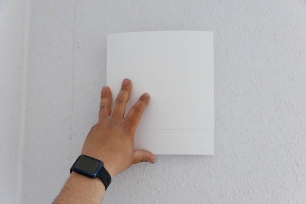 Neuer ALT-Text: "Fachhandwerker steuert ein modernes, weißes Raumthermostat an einer strukturierten Wand per Smartwatch für die smarte Heizungsregelung in der Gebäudetechnik.