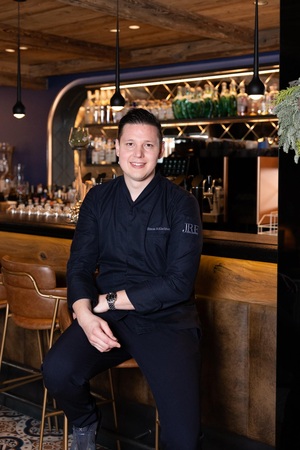 Ein Küchenchef in schwarzer Berufskleidung sitzt an einer Theke eines modernen Gastraums - Beispiel für anspruchsvolle Gastro-Gebäudetechnik.