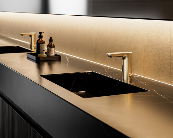 Edler Waschtisch mit schwarzem Marmorwaschbecken, goldener Armatur und Seifenspendern; energieeffiziente LED-Unterbauleuchte.