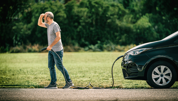 Mann hält Ladekabel in der Hand und sucht nach Ladesäule oder Ladestation für Elektroauto