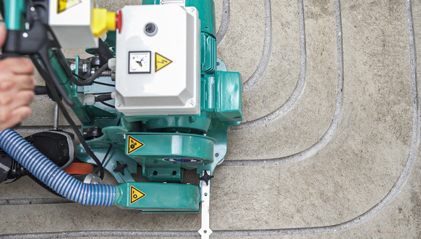 Eine Fräsmaschine bearbeitet einen Estrichboden, um eine Fußbodenheizung zu installieren.