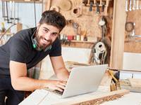 Junger Mann arbeitet in einer Holzwerkstatt am Laptop