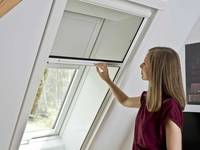 Roto Insektenschutzrolle an einem Dachfenster mit einer Frau davor, die es bedient
